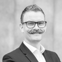 Black and white portrait of Torbjoern Netland wearing glasses and a suit